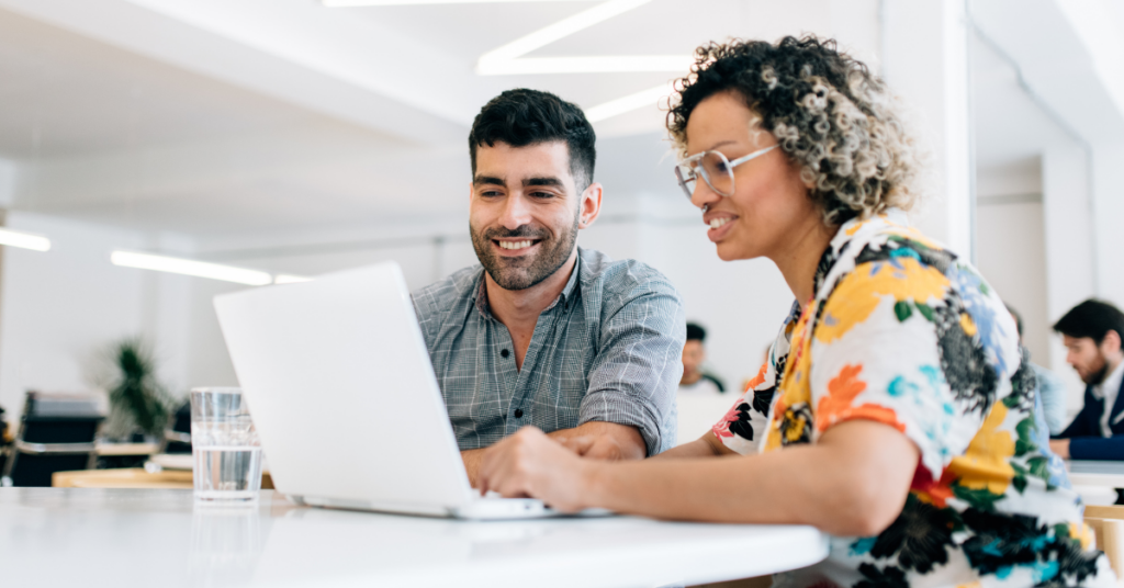 woman and man sitting at table looking at laptop screen