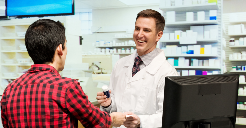 pharmacist behind counter talking to customer with medicine in hand,