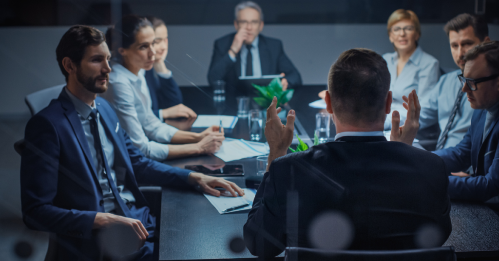 men and women in suits sitting around a meeting room table.