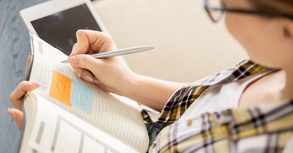 Woman writing notes and plans in a diary with post-it notes.